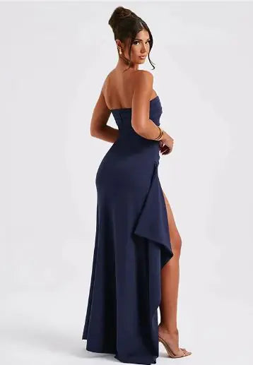 Woman wearing a strapless navy gown with a high slit on a white background